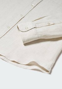 Camicia a manica lunga in lino beige con polsini abbottonati e bottoni visibili lungo la patta frontale, stesa piatta.