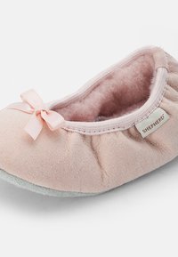 Rosa mockaskinnsballerinaskor med en mjuk, fluffig insida, dekorerad med en liten satinrosett och en grå gummisula. Varumärkesetikett synlig på sidan.