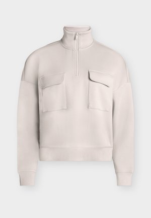 Pull-over beige clair à manches longues avec col montant, fermeture éclair frontale sur un quart, et deux grandes poches à rabat sur la poitrine.