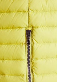 Gult quiltat tyg med horisontell sömnad och en centrerad mörk dragkedja som är delvis stängd.