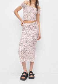 White floral crop top with off-the-shoulder sleeves and ruffled edges, paired with a matching knee-length skirt. Black platform sandals.