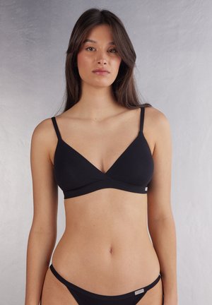 Black wireless bralette with triangular cups, thin adjustable straps, and a smooth texture. Features a subtle logo tag on the side.