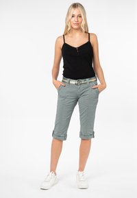 Lichtgroene cropped broek met opgerolde pijpen, voorzakken en een gemusterde tailleband. Gepaarde met een zwarte tanktop en witte sneakers.