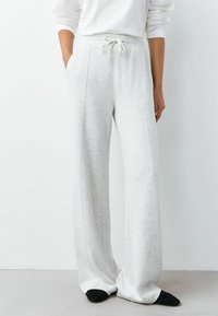 Hellgraue Sweatpants mit weitem Bein und hoher Taille, Schnürverschluss, Seitentaschen und kontrastierenden Nähten. Weicher, strukturierter Stoff.