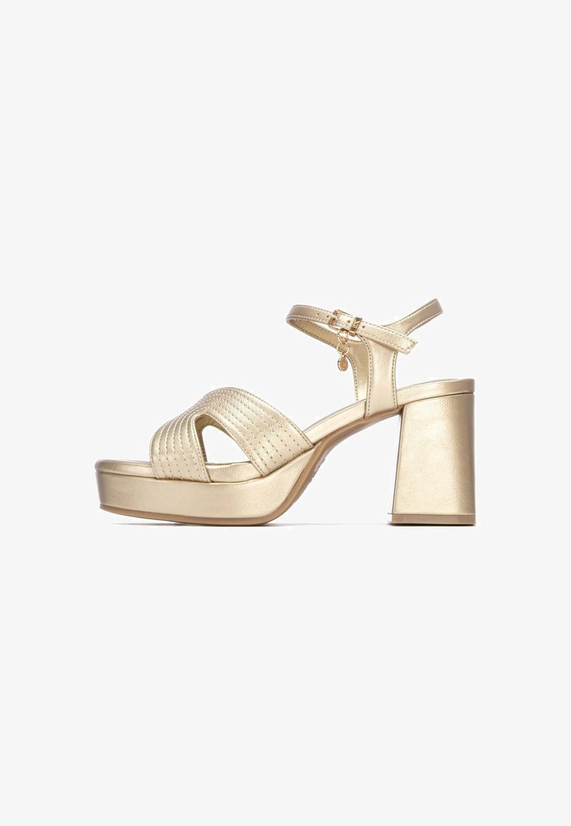 Las sandalias de plataforma dorada cuentan con un tacón ancho, una tira ancha para los dedos con textura acanalada y una correa ajustable en el tobillo con hebilla y detalle de charm.