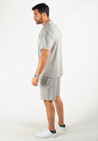Tenue de sport grise composée d'un t-shirt ample à manches courtes et d'un short assorti, fabriqués en matériau texturé, associés à des baskets blanches.