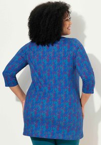 Sininen ja violetti kuvioitu tunika, jossa on kolme neljännesosaa hihat, pehmeä kangas, rento istuvuus ja pyöristetty helma, joka ulottuu lantion alle.