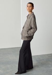 Gray plaid jacket with a collar, front pocket, and gathered hem, paired with black flared pants and pointed black shoes.