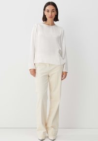 Blusa bianca a maniche lunghe con scollatura rotonda abbinata a pantaloni a zampa d'elefante in corduroy crema. Tessuto morbido, design su misura e tonalità neutre.