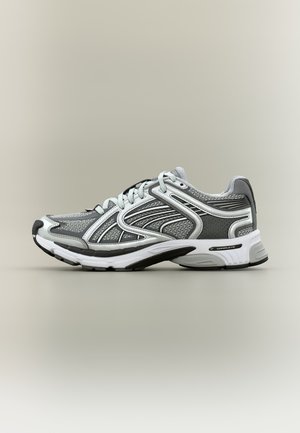 Harmaa ja valkoinen urheilukäyttöön tarkoitettu juoksukenkä verkkokankaalla, synteettisillä päällysteillä ja pehmustetulla pohjalla neutraalilla taustalla.