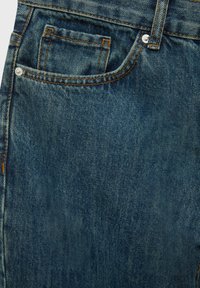 Gros plan sur la poche avant d'un jean en denim bleu avec des surpiqûres orange et des rivets métalliques.