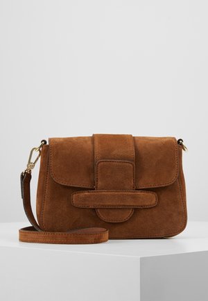 Brun ruskind crossbody taske med klaplukning og bred remdetalje, guldfarvet hardware og justerbar skulderrem, hviler på en hvid overflade.