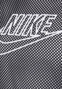 Czarna siateczkowa tkanina z wyraźnym białym logo Nike ze wzorem Swoosh, prezentująca teksturowany wzór małych otworów na całej powierzchni.