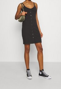 Gray ribbed dress with button-down front, thin straps, and a fitted design, complemented by black high-top sneakers and a small green bag.