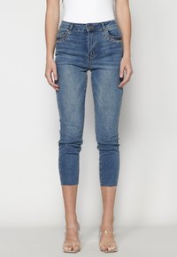 Jeans ajustados de denim azul. Presentan costuras decorativas cerca de los bolsillos, una longitud recortada y un dobladillo ligeramente deshilachado.