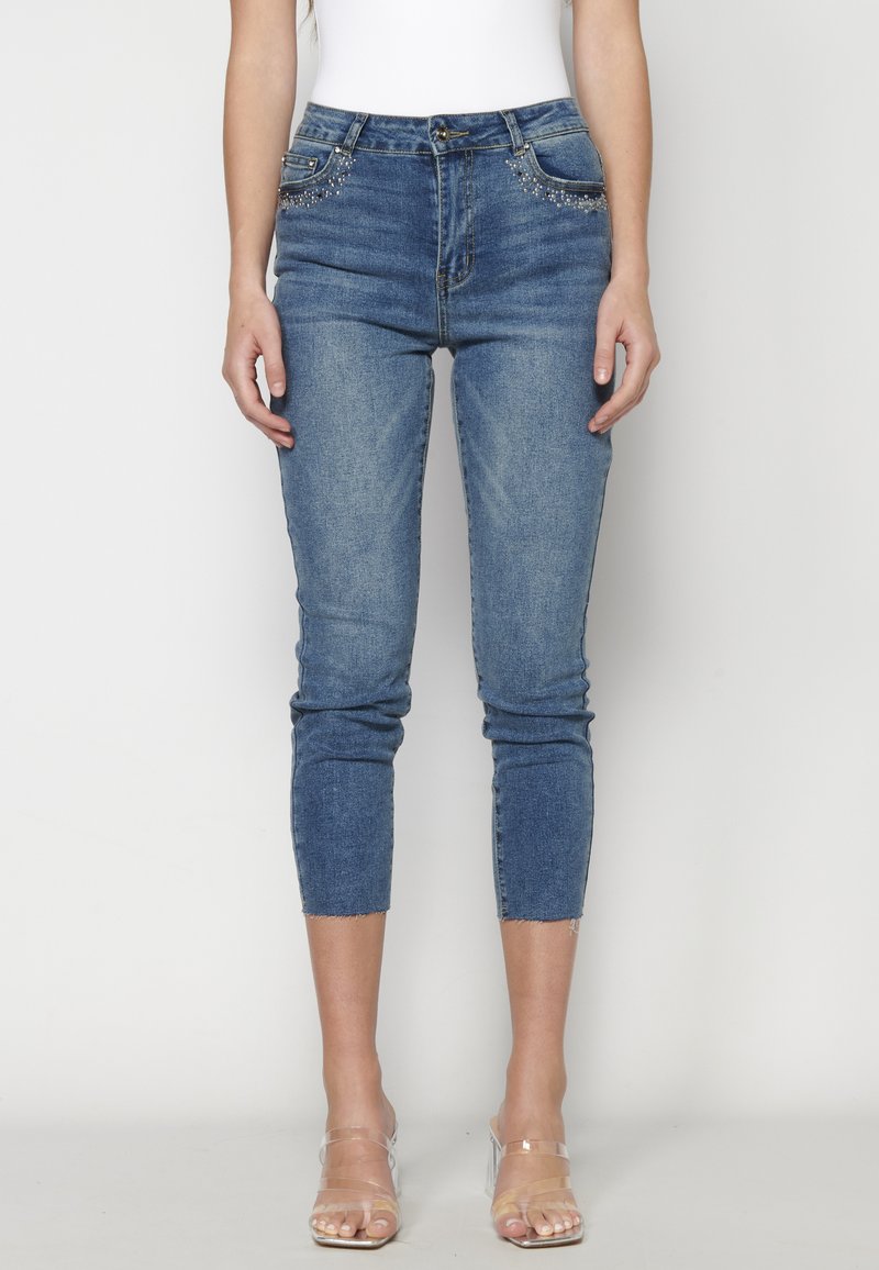 Jeans ajustados de denim azul. Presentan costuras decorativas cerca de los bolsillos, una longitud recortada y un dobladillo ligeramente deshilachado.
