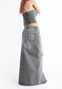 Grijze denim maxi rok met een aansluitende taille, voorzien van een split aan de achterkant en subtiele stiksel details. Gladde textuur met een lichte glans.