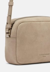 Borsa a tracolla in suede beige con chiusura a zip, texture liscia, angoli arrotondati e logo impresso sul davanti. Tracolla regolabile per maggiore comodità.
