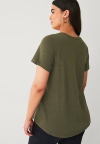 Olivengrøn, T-shirt med korte ærmer og rund kant samt blød tekstur, vist fra ryggen, båret med mørke bukser.