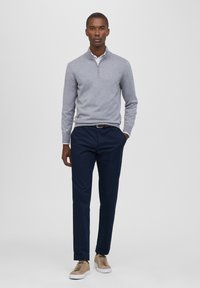 Grauer langärmeliger Pullover mit Reißverschlusskragen, kombiniert mit marineblauen Hosen und hellbraunen Sneakers. Glatte Textur mit passgenauer Design.