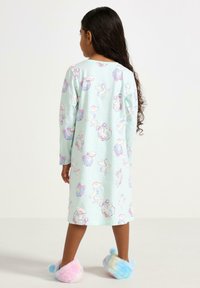 Mintgrünes Nachthemd mit langen Ärmeln, das ein verspieltes Einhorn- und Wolkenmuster zeigt. Weicher Stoff, der bis zur Mitte der Wade reicht, kombiniert mit pastellfarbenen, flauschigen Hausschuhen.