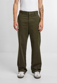 Olijfgroene wijde broek van katoen, met een knoopsluiting, zijzakken en een gladde textuur. Ggedragen met witte sneakers.