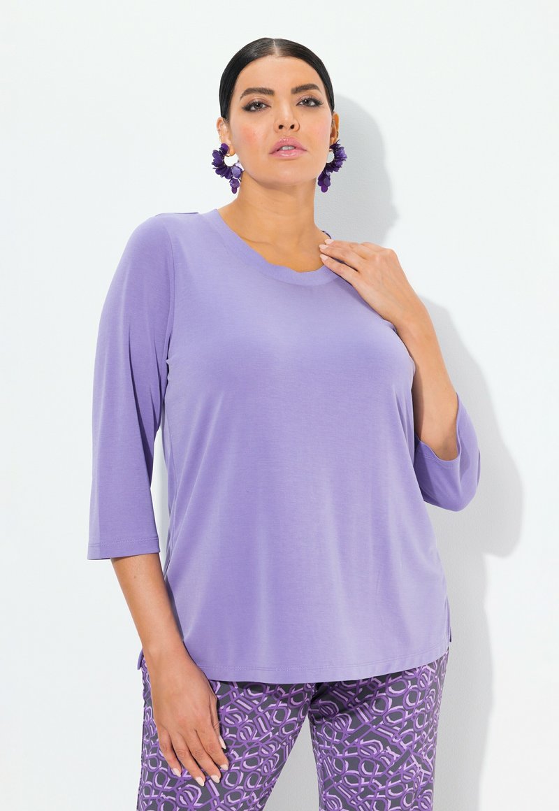 Lila, locker sitzendes Oberteil mit Rundhalsausschnitt und drei Viertelärmeln. Kombiniert mit gemusterten lila Hosen mit geometrischen Designs.