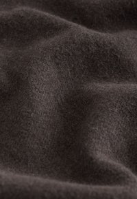 Tissu en laine brun foncé avec une texture douce et duveteuse et de légers plis créant des ombres et des reflets subtils.