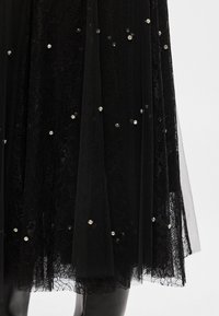 Μαύρη φούστα από τούλι με επικάλυψη δαντέλας, διακοσμημένη με διάσπαρτους στρας. Ροή και στρωματοειδής υφή.