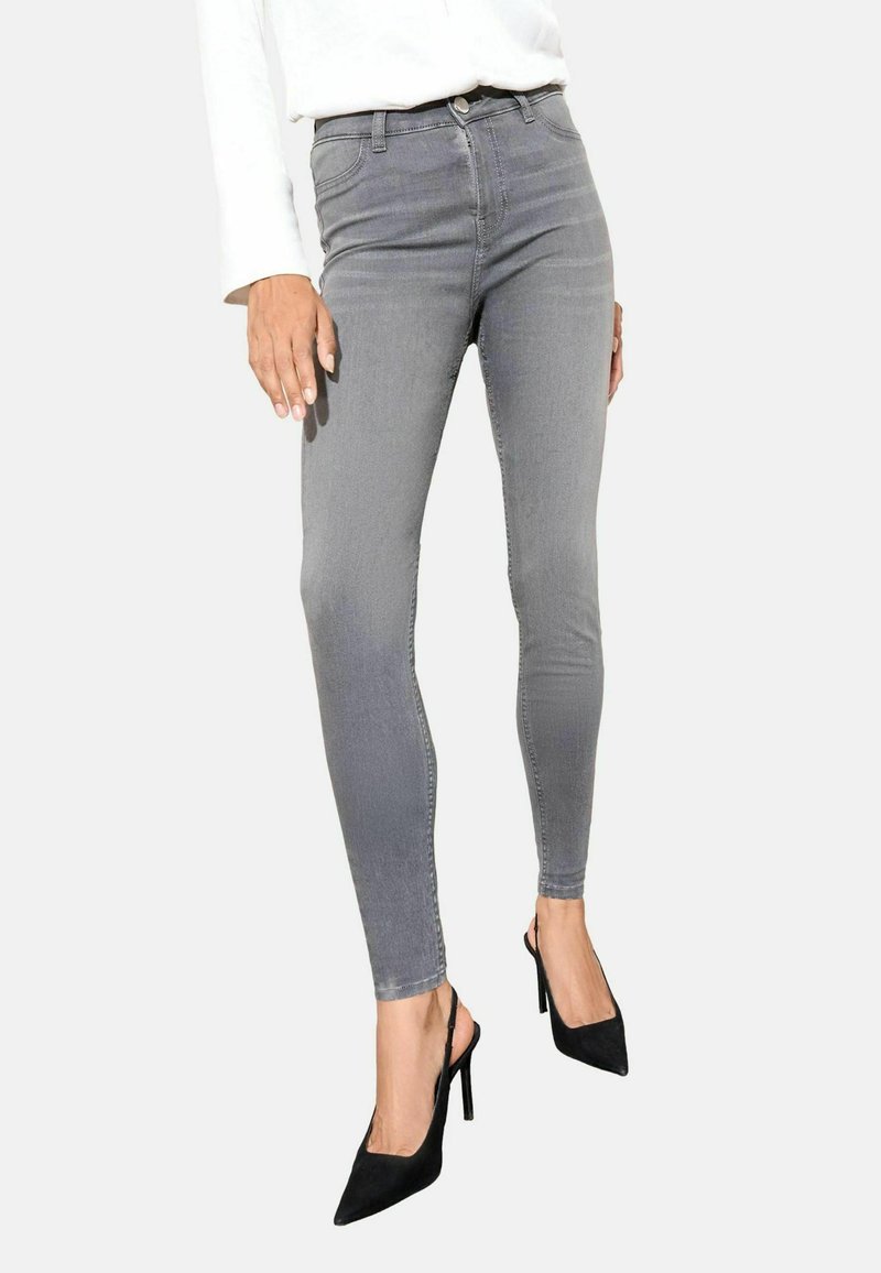 Szürke, slim fit farmernadrág sima textúrával, magas derékkal, öt zsebes dizájnnal és enyhe kopással, fekete, hegyes orrú magassarkúval párosítva.