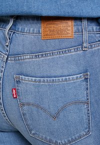 Jeans de mezclilla azul claro con un parche de cuero en la parte trasera que incluye "Levi Strauss & Co." Dos bolsillos traseros y una etiqueta roja de Levi's visible.