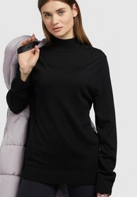 Svart polotröja i mjukt stickat material, med långa ärmar och ribbat nederkant. Rosa puffjacka hängande över ena axeln.
