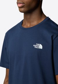 Navy sininen puuvillapaita lyhyillä hihoilla ja pyöreällä kaula-aukolla, jossa on valkoinen "The North Face" -logo vasemmassa rinnassa.