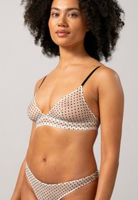 Ensemble de soutien-gorge et bikini en tissu beige transparent avec des pois noirs. Présente des bretelles noires fines et une texture lisse avec un design triangulaire.