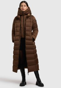 Brun pufferjakke med hætte, der har et quiltet design og høj krave. YKK lynlås-lukning, sidelommer og en lang, lige silhuet.