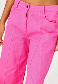 Jasnoróżowe dżinsy z wysokim stanem, z zamkiem błyskawicznym, zapięciem na guzik i kieszeniami po bokach. Gładka tekstura z widocznym przeszyciem.