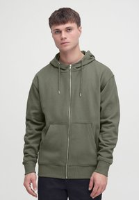 Õlivihreast pehmest puuvillasegust materjalist tõmblukuga joped, millel on kapuuts paelaga, esitaskud ning soonikkoes mansetid ja serv.