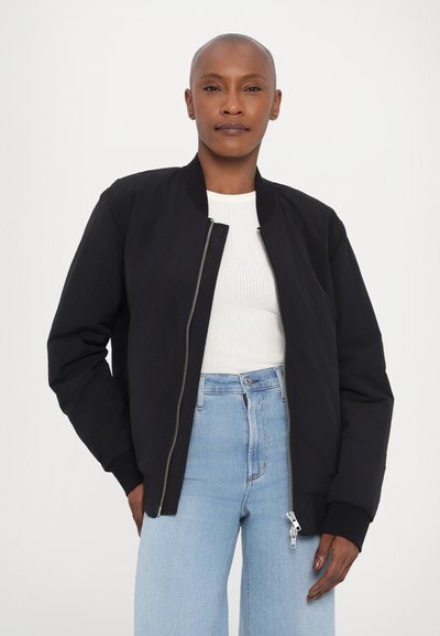 Juodas bombonešis su priekyje užtrauktuku, raukšlėta apykakle ir rankovėmis. Dėvimas ant baltos raukšlėtos maikutės, derinamas su šviesiai mėlynomis plačiomis kelnėmis.