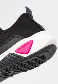 Mustat urheilukengät, joissa on sileä kankainen päällinen, valkoinen välipohja ja teksturoitu musta kumipohja. Ominaisuutena vaaleanpunainen kolmion muotoinen korostus.