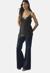 Zwarte satijnen cami met kantafwerking bij de halslijn, gecombineerd met donkere, uitlopende jeans. De outfit heeft dunne bandjes en een comfortabele pasvorm.