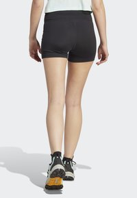 Svarte treningsshorts med høy midje, glatt tekstur og minimale sømdetaljer, sammen med svarte og mintgrønne joggesko.