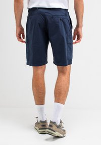 Marineblauwe cargoshorts van lichtgewicht stof met meerdere zakken en een ontspannen pasvorm, gecombineerd met grijze sneakers en witte sokken.