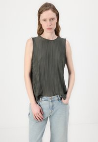 Ermeløs grønn plissébluse med rund hals. Myk tekstur og flytende design, sammen med lyseblå høyhøyde jeans.