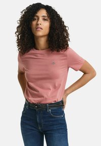 Roze t-shirt met korte mouwen van zachte stof, met een klein logo op de borst. Gecombineerd met donkerblauwe jeans en een zwarte riem.