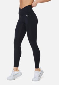 Hoge zwarte leggings met een gladde textuur, voorzien van een logo aan de linkerkant en een aansluitend ontwerp voor optimale ondersteuning.