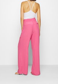Pantalons larges roses avec une taille haute, fabriqués dans un tissu léger. Présentent une texture lisse et deux poches arrière.