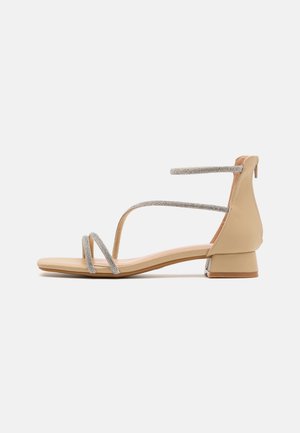Sandales beige au design minimaliste, avec des brides pailletées argentées et un petit talon carré. Matière supérieure lisse et semelle plate.