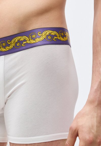 Ανδρικός κορμός που φοράει λευκά μποξεράκια με μοβ μέση που διαθέτει κίτρινο μοτίβο με φυλλώδη σχέδια.