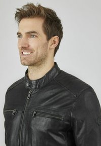 Giubbotto di pelle nera con colletto alto, chiusura lampo anteriore e due tasche con zip. Presenta un design delle spalle trapuntato e una texture liscia.