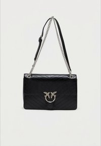 Mala preta em pele acolchoada com um fecho circular prateado decorado com dois pássaros. Possui uma alça de corrente destacável e uma alça de ombro em pele.